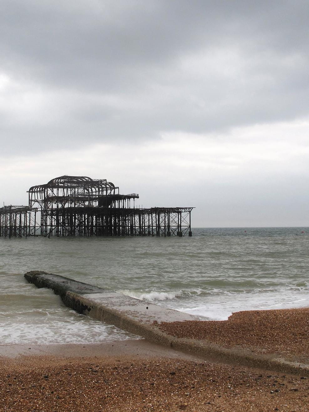 A view from the beach to Brighton West Pier with a footbridge on a cloudy day