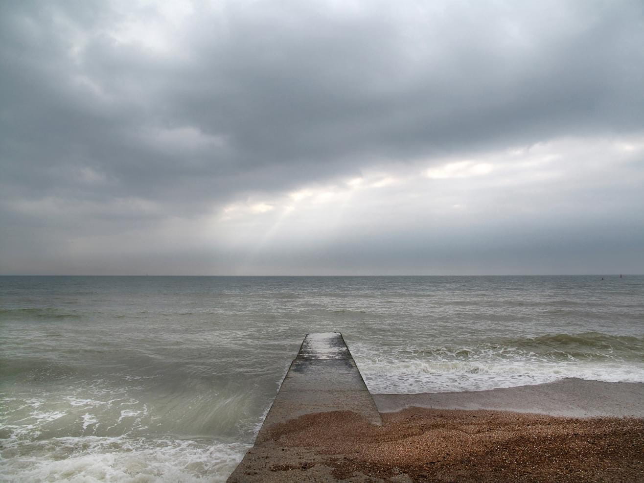 A view from the Brighton beach to the sea with a footbridge on a cloudy day